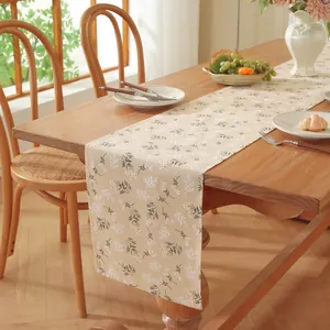 Détail d'un chemin de table crème avec motifs floraux verts sur une table en bois