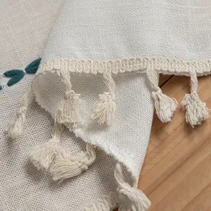Close-up of beige linen fabric with tassel fringe and green leaf embroidery detail