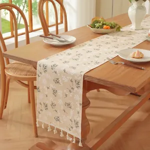 Détail d'un chemin de table fleuri avec franges crème et motif de feuilles vertes