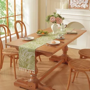 Détail du chemin de table vert avec motifs de feuilles blanches et pompons en coton