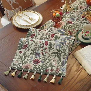 Dettaglio del runner jacquard floreale con nappe boho su un tavolo di legno rustico