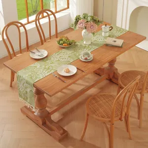 Chemin de table vert avec motifs de fougères et pompons blancs sur table en bois