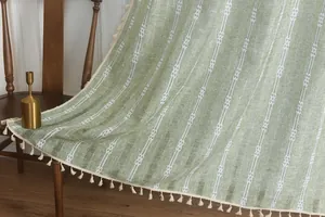 Close-up of light green striped polyester fabric with elegant cream white tassels