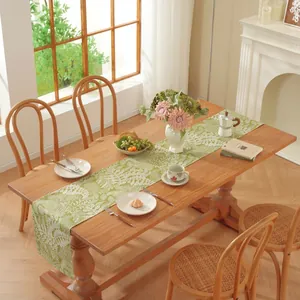 Détail du chemin de table vert avec imprimés floraux blancs sur une table en bois