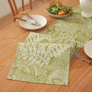 Détail du chemin de table vert avec motif de feuilles blanches sur table en bois