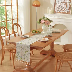 Détail d'un chemin de table crème avec motifs floraux et franges blanches sur table