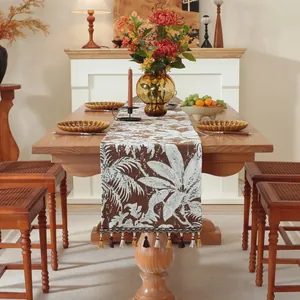 Runner da tavola jacquard marrone con motivi a foglie e nappe su tavolo in legno