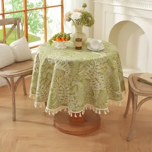 Détail d'une nappe ronde verte à motifs de feuilles et franges à glands beiges