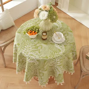 Détail de nappe ronde verte avec motif de feuilles et franges de pompons blancs