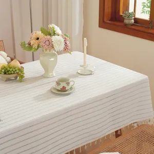 Détail d'une nappe à rayures crème avec pompons blancs sur une table à manger en bois