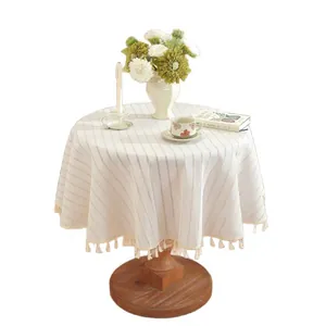 Minimalist round tablecloth with beige stripes and fringe tassels on a wooden table