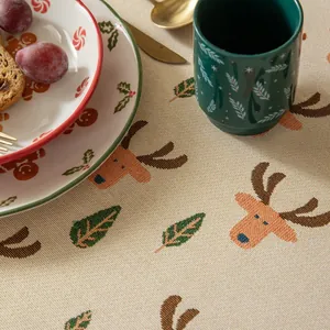 Detailed close-up of beige Christmas tablecloth with orange reindeer and green pine patterns