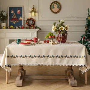 Beige Christmas tablecloth with reindeer patterns, snowflakes, and white pom-pom tassels