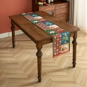 Dettaglio del runner da tavola natalizio con motivi Babbo Natale e nappe a pompon rossi