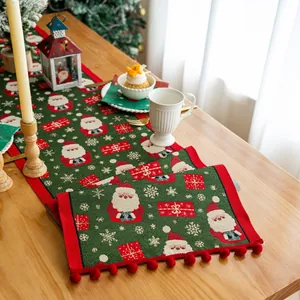 Dettaglio del runner natalizio verde con frange a pompon su un tavolo da pranzo in legno