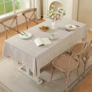 Detalle de mantel de lino sintético gris claro con patrón de cuadros blancos y borlas