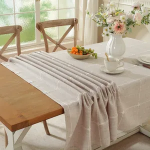 Detalle de mantel de lino sintético beige con bordado de rejilla blanca y flecos elegantes