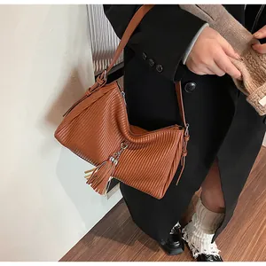 Detail of brown pleated tote bag featuring a leather tassel and metallic chain strap