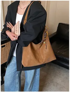 Detail van bruine suède-look tote tas met gouden logoplaatje en decoratieve kwastjes