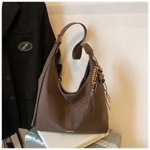 Detail van een bruine hobo-tas met etnische houten kralen en lederen kwastjes als decoratie