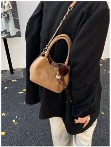 Secchiello in camoscio marrone con catena dorata e pompon decorativo su foglie di ginkgo