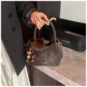 Dettaglio borsa a secchiello marrone scuro con scritte oro, pompon e nappine