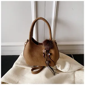 Dettaglio borsa a secchiello marrone con nappa e logo dorato su tessuto bianco