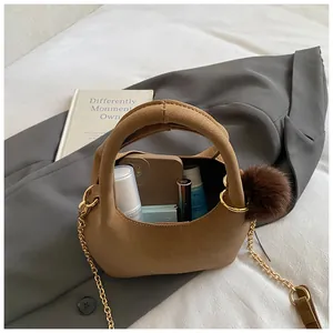 Borsa a secchiello marrone in similpelle con catena dorata e ciondolo a pompon su sfondo