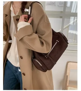 Detailed view of deep brown suede cylinder crossbody bag with silver hardware and zippers