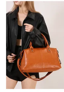 Modell mit großer orangefarbener Boston-Tasche aus Kunstleder mit Umhängegurt über Jacke