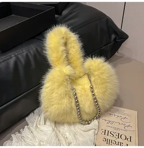 Detail of bright yellow plush handbag with silver beaded chain on a chic leather surface