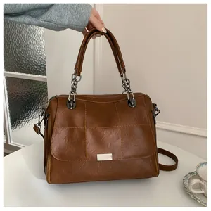 Macro detail of brown retro leather handbag featuring square stitching and metal chain