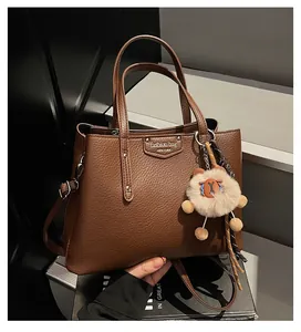 Detail of brown litchi pattern leather bag with metal nameplate and plush pendant