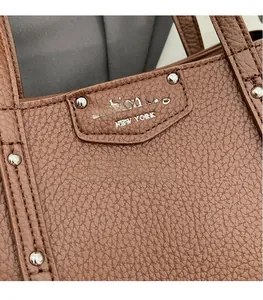 Macro shot of brown lychee grain leather texture with silver rivets and fashion logo