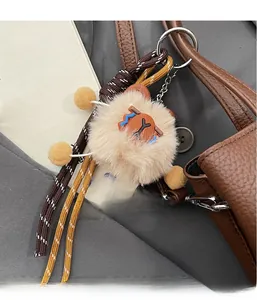Detail of plush bear charm with woven rope and pom-poms hanging on brown leather bag