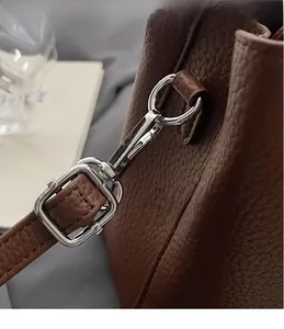 Close-up of silver metal hooks and buckle on brown lychee texture leather handbag