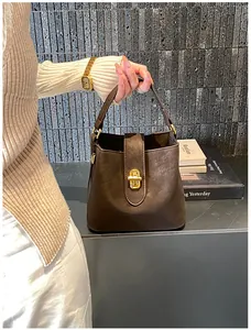 Detail of a brown leather bucket bag with a golden twist lock held by a model