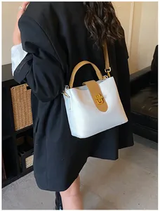 Detail of a white and brown contrast bucket bag with gold twist-lock and shoulder strap
