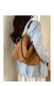 Caramel brown leather tote bag with chain strap detail shown on model in a soft blue suit