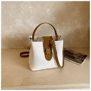 Detail of white bucket bag with brown leather straps and gold metal twist lock closure