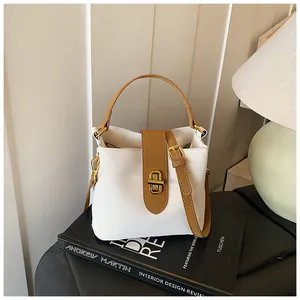 White bucket bag with brown leather trim and golden metal clasp on a minimalist background