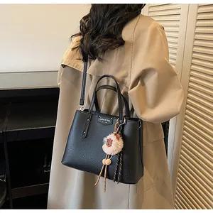 Detail of black lychee grain leather handbag with plush ball charm and silver nameplate