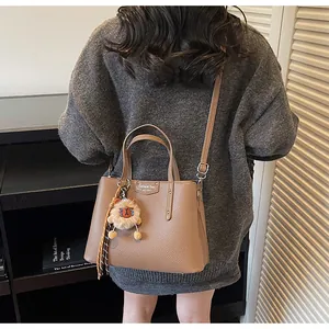 Lifestyle view of a brown textured crossbody bag with a plush lion charm on a bookshelf