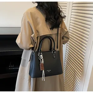 Détail d'un sac à main noir en cuir grainé avec poignée métallique et pendentif mode