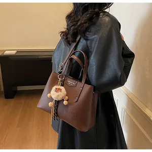 Detail of dark brown lychee textured leather tote bag with a cute plush bear pendant