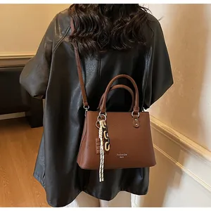 Détail du sac à main marron en cuir grainé avec pendentif et finitions argentées