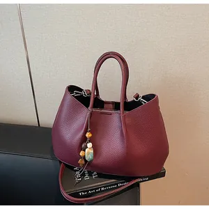 Detail der weinroten Shopper-Tasche aus Narbenleder mit Perlenanhänger und Griffen