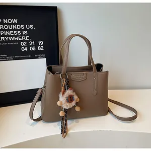 Detailed view of brown litchi grain leather handbag with cute sheep pendant on white podium
