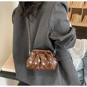 Borsa nuvola arricciata marrone con borchie argentate indossata con completo grigio