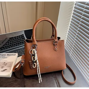 Sac à main marron en cuir texturé avec anses rondes et pendentif de mode sur bureau
